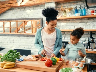 Cute black girl assisting her mother in preparing food in the kitchen.