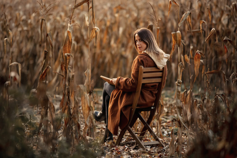 Style woman with book sitting on chair on corn field in autumn time season