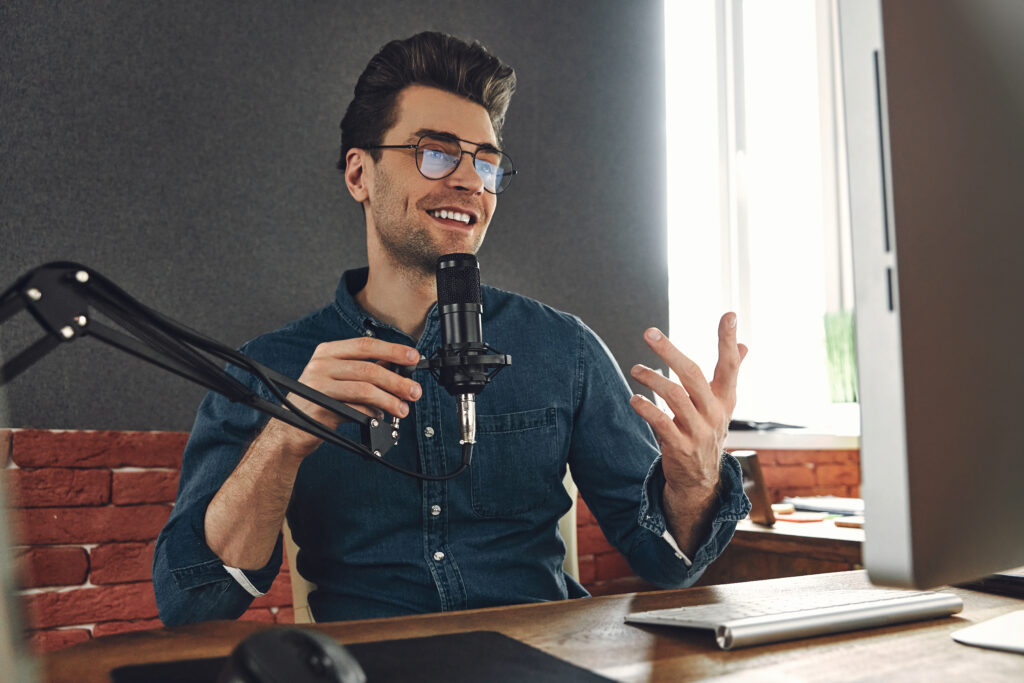 Happy young man using microphone and gesturing while recording podcast in studio