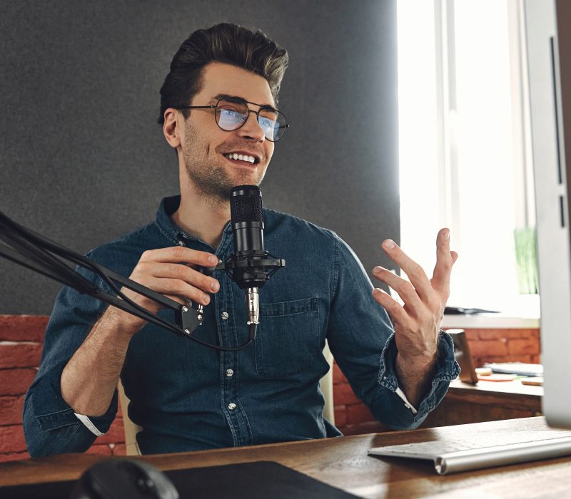 Happy young man using microphone and gesturing while recording podcast in studio