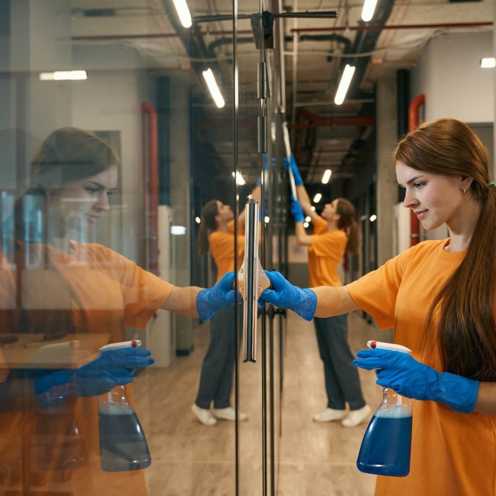Two young employees cleaning company clean mirrored surfaces coworking space
