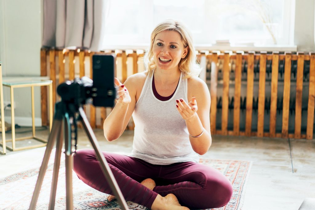 Athletic female fitness and yoga blogger in sportswear recording video of training on mobile